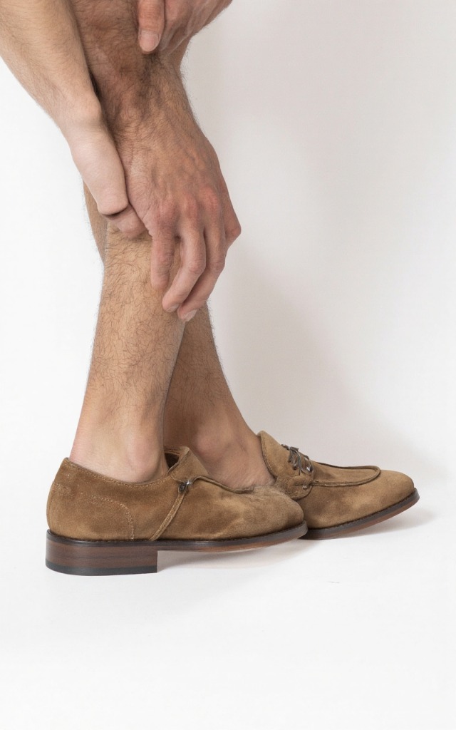 A male model wearing Suede shoes, against a white background, with a close   up of the feet
